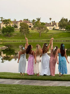 four girls standing in front of a lake with their arms up and one girl holding her hand out