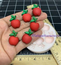 a person is holding some tiny red fruit shaped magnets on their thumb and finger