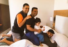 three men and two children sitting on top of a bed in a room with white walls