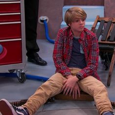 a young man sitting on top of a wooden bench in front of a tv set