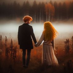 a man and woman holding hands while standing in a field with foggy trees behind them