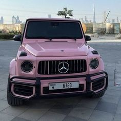 a pink mercedes g - class is parked on the street