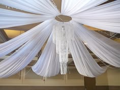 a chandelier hanging from the ceiling with white drapes and lights on it