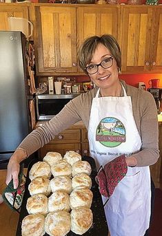 a woman in an apron holding a tray of doughnuts