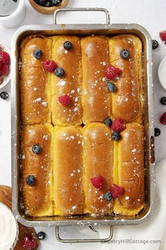 a pan filled with rolls covered in berries and powdered sugar on top of a table