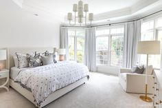 a bedroom with white walls and carpeted flooring has a large bed in front of two windows