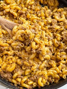 a skillet filled with macaroni and cheese being stirred by a wooden spoon