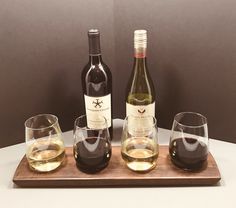 three wine glasses and two bottles on a wooden tray