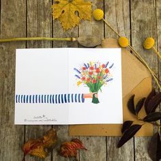 a card with flowers on it sitting next to some leaves and acorny plants