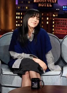 a woman sitting on top of a couch next to a table with a coffee cup