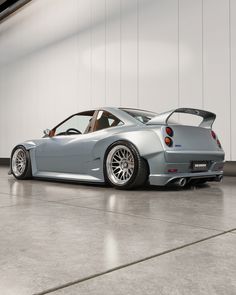 a silver sports car parked in front of a white wall and some concrete flooring