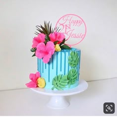 a blue cake decorated with pink flowers and palm leaves