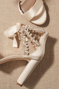 a pair of high heeled shoes with bows and pearls on the side, next to a satin ribbon