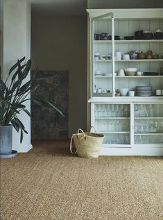 a basket sitting on the floor in front of a book shelf with dishes and bowls