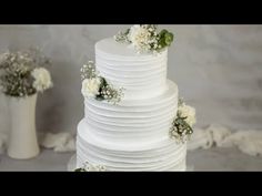 a white wedding cake with flowers on the top and bottom tier is sitting in front of two vases