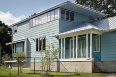 a house with blue siding and white trim on the windows, sitting in front of a fenced yard