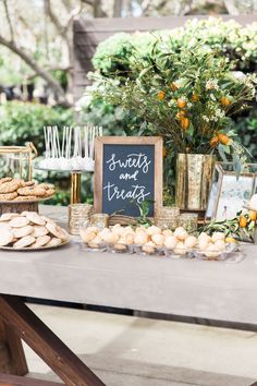 a table topped with cookies and pastries next to a chalkboard sign that says sweets and treats