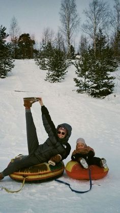 two people laying in the snow on sleds with one person holding onto another