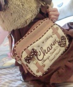 a teddy bear wearing a brown shirt and holding a purse with the name charm on it