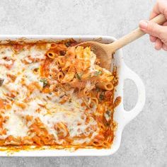 a person holding a wooden spoon over a casserole dish filled with pasta and sauce