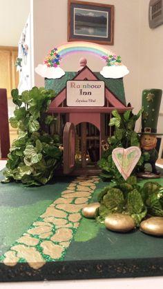 a green table topped with lots of leafy plants next to a small wooden house