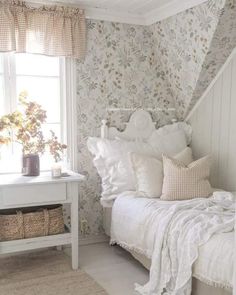 a white bed sitting next to a window in a room with floral wallpaper on the walls