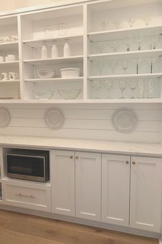 a kitchen with white cabinets and glassware on the shelves