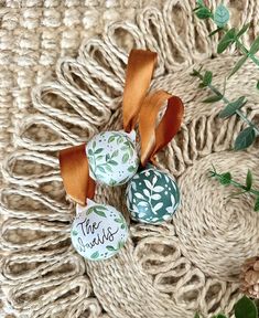 three ceramic ornaments with ribbons on top of a woven blanket and green leaves around them