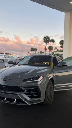 a grey lamb car parked in front of a building with palm trees and other cars