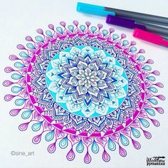 a drawing of a colorful flower on paper with markers and marker pens next to it