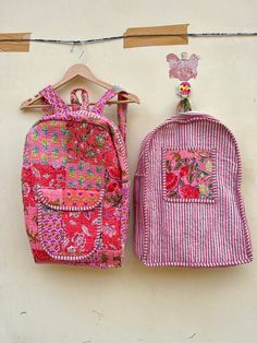 two backpacks are hanging on a clothesline and one has a patchwork pocket