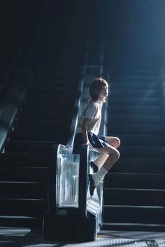 a woman sitting on top of an escalator next to a hand rail in the dark