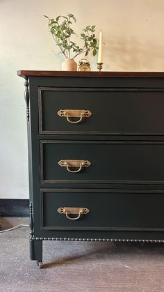 a black dresser with brass handles and knobs on the bottom drawer, next to a potted plant