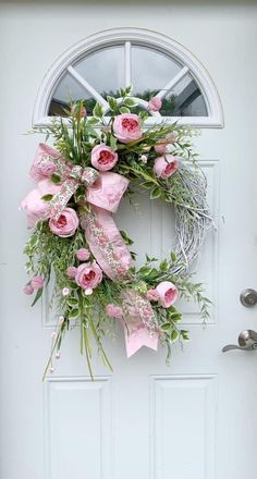 a wreath with pink flowers and greenery hangs on the front door