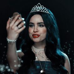 a woman wearing a tiara and holding a ring in front of her face while smiling