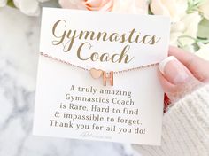 a person holding a card that says gymnastics coach with a heart on it and flowers in the background