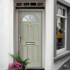 a green front door on a white house with pink flowers in the window sill