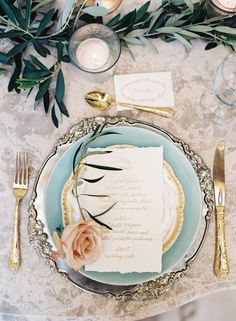 an elegant table setting with place settings and gold cutlery, silverware, and greenery