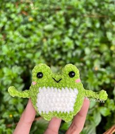 a hand holding up a small green frog brooch with white teeth and black eyes