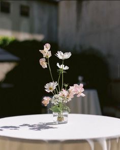 a vase filled with flowers sitting on top of a white table cloth covered round table