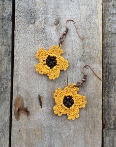 two yellow crocheted flower earrings hanging from hooks on wooden planks with earwires