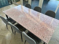 a dining room table with chairs and a large pink marble slab on the top, in front of a glass door