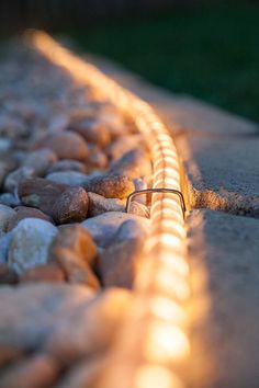 the light is shining on some rocks and grass in front of a stone wall with a wire running through it