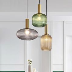 three different colored glass pendant lights hanging from the ceiling above a table with flowers and vases on it