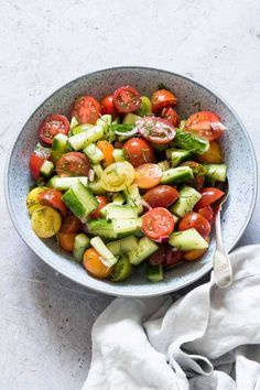 a bowl filled with cucumber, tomatoes and other vegetables on top of a table