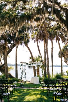 an outdoor ceremony set up with chairs and tables in front of the water, surrounded by trees