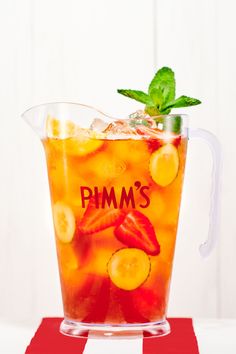 a pitcher filled with fruit and ice sitting on top of a red tablecloth next to a white wall