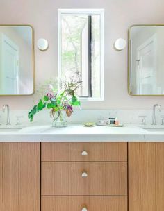 a bathroom with two sinks, mirrors and a vase full of flowers on the counter