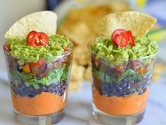 a glass filled with black beans, guacamole and tortilla chips