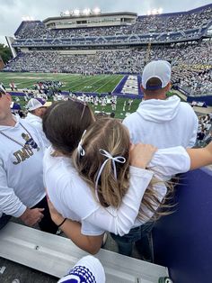 two people sitting in the bleachers at a football game, hugging each other